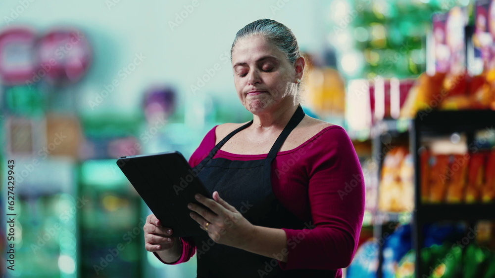 Stressed female entrepreneur owner of small business struggling with hard times holding tablet and staring at the bottom line of the grocery store Stressed female entrepreneur owner of small business struggling with hard times holding tablet and staring at the bottom line of the grocery store