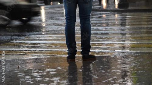 Close-up view of male person standing by crosswalk while cars drives on city street during heavy rain. Bad weather. Soft focus. Real time video. Transportation theme.