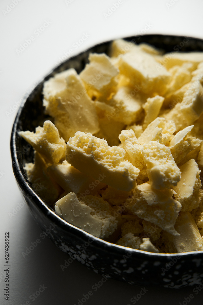 Broken white chocolate in a black ceramic bowl. The main ingredient for making blondies. White marble background. Close up. Broken white chocolate in a black ceramic bowl. The main ingredient for making blondies. White marble background. Close up.