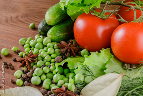A set of several cucumbers, pea, dill, lettuce, tomato branch, bay leaf, pepper, anise, lie on the wooden table. Fresh raw organic vegetables closeup.
