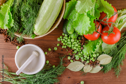 Fresh raw organic vegetables. A set of several cucumbers, dill, lettuce, tomato, zucchini, pepper, anise, bay leaf, spices, green peas lie on the wooden table. Closeup. Top view.