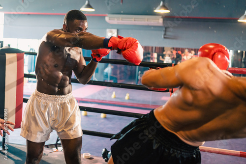 Young muscular african american male boxer looking at camera, wearing boxing gloves, standing isolated over grey background. Sports, workout and bodybuilding concept, confident african american boxer