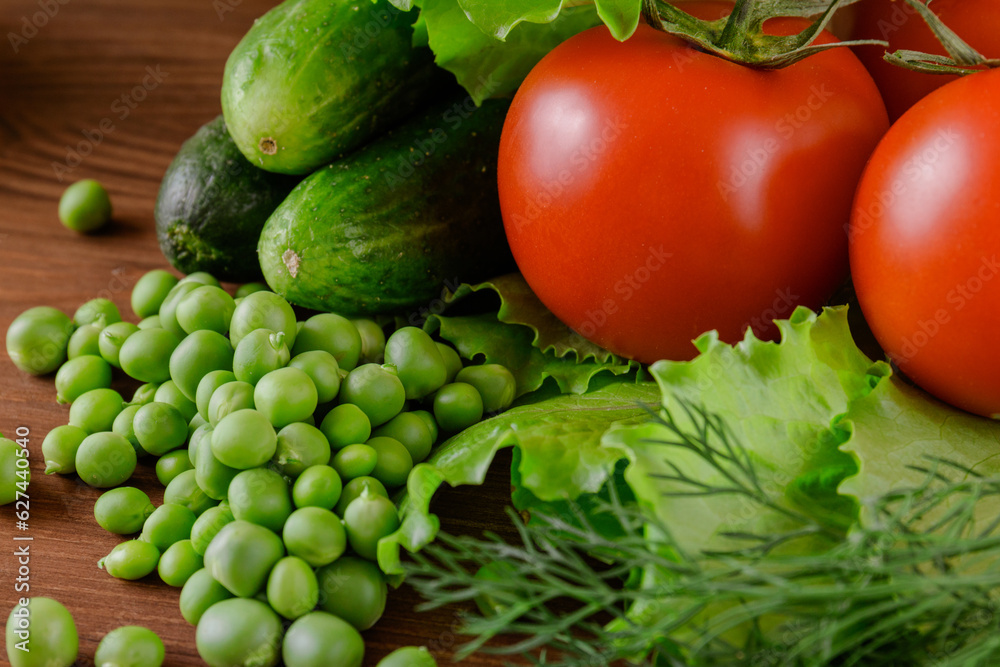 A set of several cucumbers, pea, dill, lettuce, tomato branch lie on the wooden table. Fresh raw organic vegetables closeup. A set of several cucumbers, pea, dill, lettuce, tomato branch lie on the wooden table. Fresh raw organic vegetables closeup.