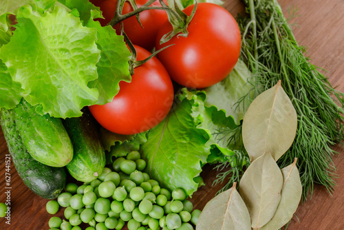 A set of several cucumbers, pea, dill, lettuce, tomato branch, bay leaf lie on the wooden table. Fresh raw organic vegetables closeup.