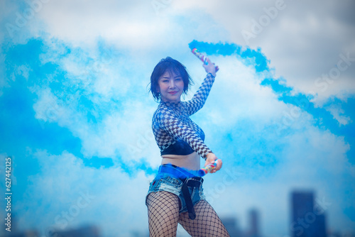 Beautiful Asian female hip hop dancer striking a sexy dance pose, attractive sexy dancer women dancing with colored smoke bomb on rooftop with skyscraper city view, hip hop street dance