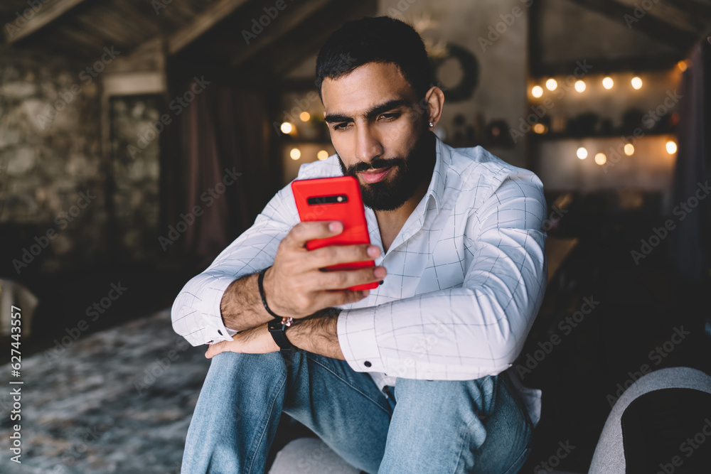 © BullRun - Thoughtful man using smartphone and sitting on sofa