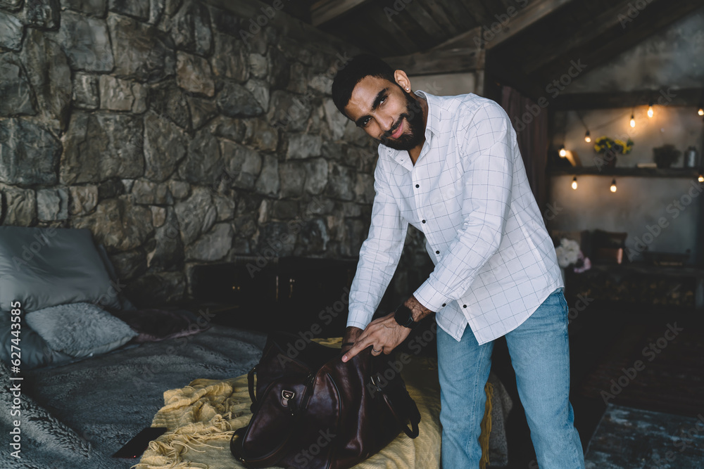Delighted man unpacking luggage near bed Delighted man unpacking luggage near bed