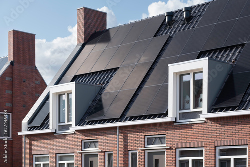 Solar panels mounted on the roofs of a row modern new-build social rental houses in Lemmer, Friesland, the Netherlands with blue sky
