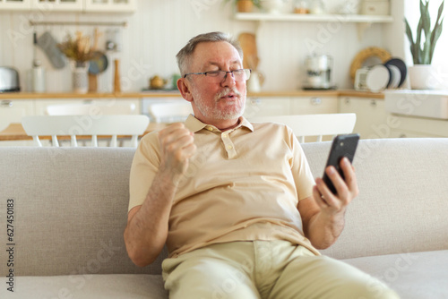 Middle aged senior man euphoric winner with smartphone. Older mature grandfather looking at cell phone reading great news getting good result winning online bid feeling amazed. Winning gesture