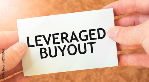 LEVERAGED BUYOUT word inscription on white card paper sheet in hands of a businessman. recap concept. red and white paper