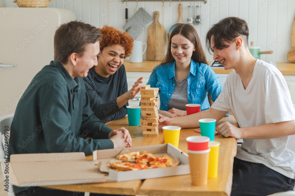 Home party. Friends spending time together playing in board game crash wooden tower at home. Happy diverse group having fun together indoor. Mixed race young buddies best friends enjoying weekend Home party. Friends spending time together playing in board game crash wooden tower at home. Happy diverse group having fun together indoor. Mixed race young buddies best friends enjoying weekend