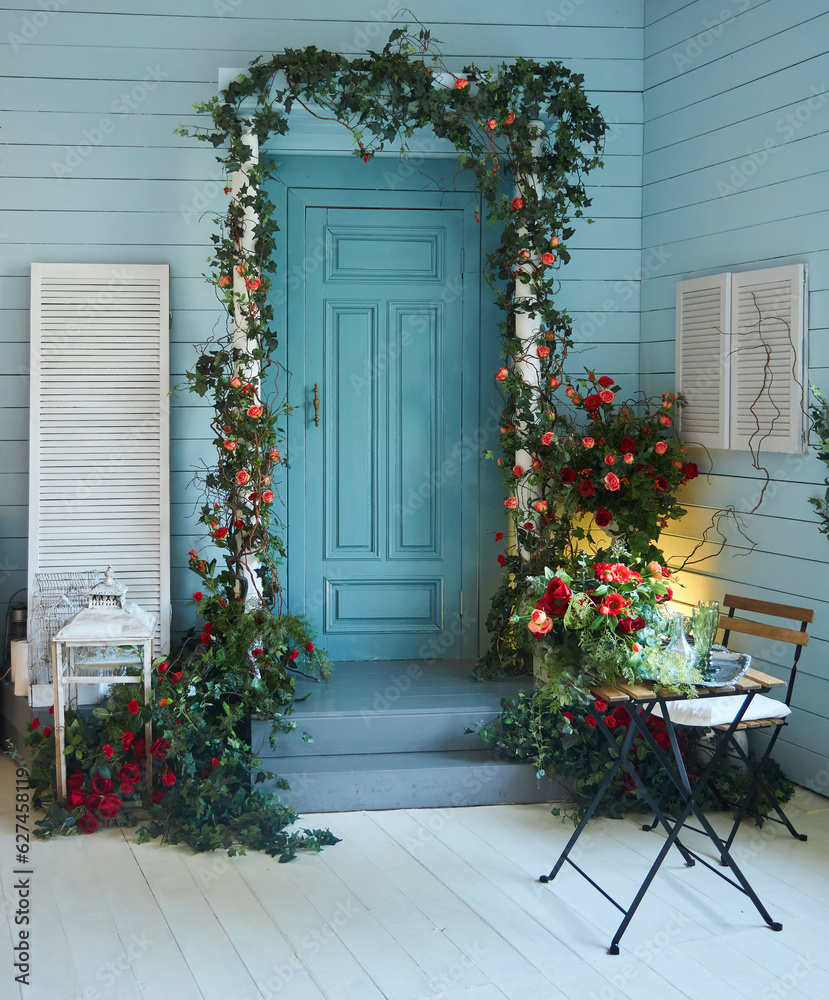 Entrance door decorated with flowers and a table. The veranda of the house in a rustic style