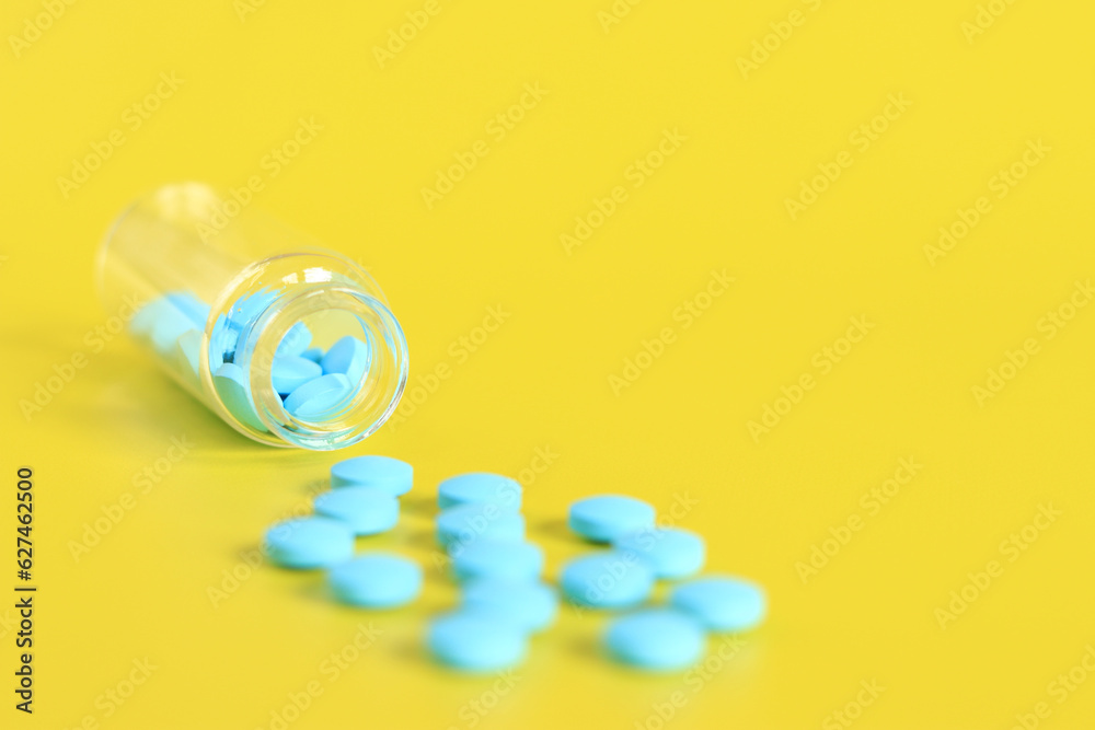 Blue pills are poured out of a glass bottle on a yellow background. Vitamin complex, side view, copy space. Healthcare, medical pills and dietary supplements Blue pills are poured out of a glass bottle on a yellow background. Vitamin complex, side view, copy space. Healthcare, medical pills and dietary supplements