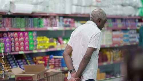 Back of a senior customer browsing at products at grocery store, looking at items to buy on shelf. Elderly shopper in candid scene, consumer lifestyle photo