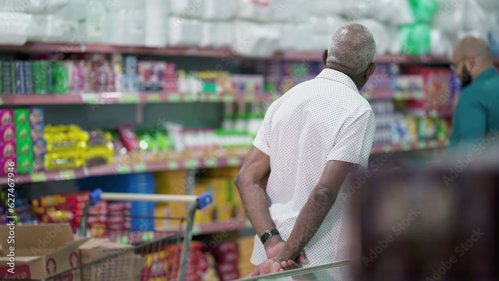 Back of a senior customer browsing at products at grocery store, looking at items to buy on shelf. Elderly shopper in candid scene, consumer lifestyle
