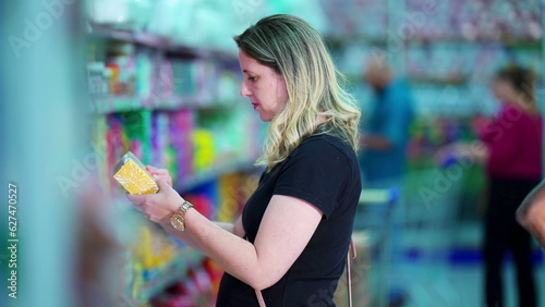 Woman selecting item from grocery shelf. Female customer seeking product while shopping, consumer lifestyle