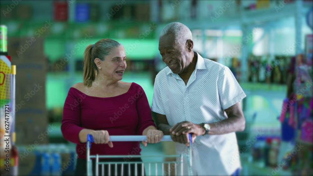 Grocery shoppers laughing and smiling, authentic candid happy middle-aged woman laughs while conversing with a senior black man posing with shopping cart at supermarket