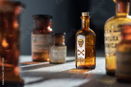 Poison bottle with skull and bones stands among pharmaceutical bottles. Danger sign, symbol of death. Concept background on poison poisoning, pharmaceutical, chemistry, medical, old science topic. photo