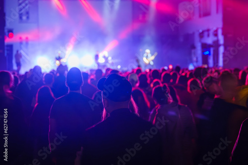 Unrecognizable crowd of people standing and listening to music of artists on stage in concert