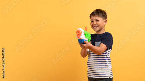 Happy little preteen boy in summer clothes holds water gun photo