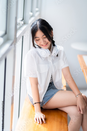 Happy of cute smiles Asian of attractive young Cute little girl wearing white wireless headphones and listening music enjoying favourite audio at the cafe on vacation at a coffee shop.