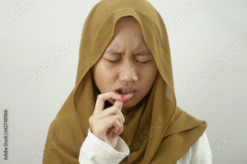 Portrait of Asian muslim teenage girl wearing hijab touching her lips, suffering from mouth sore or aphtha photo