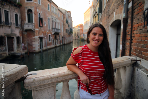 A girl in a red shirt with white lines posing in front of a canal in Venice, Italy