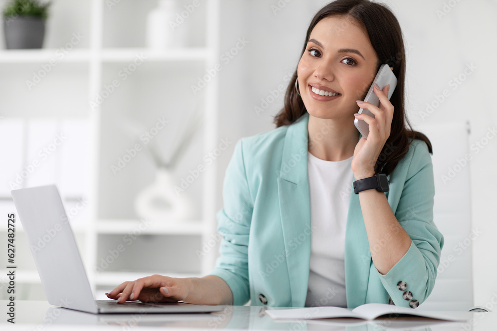 Smiling pretty millennial caucasian woman manager in suit typing on computer, calls by phone, enjoy work Smiling pretty millennial caucasian woman manager in suit typing on computer, calls by phone, enjoy work