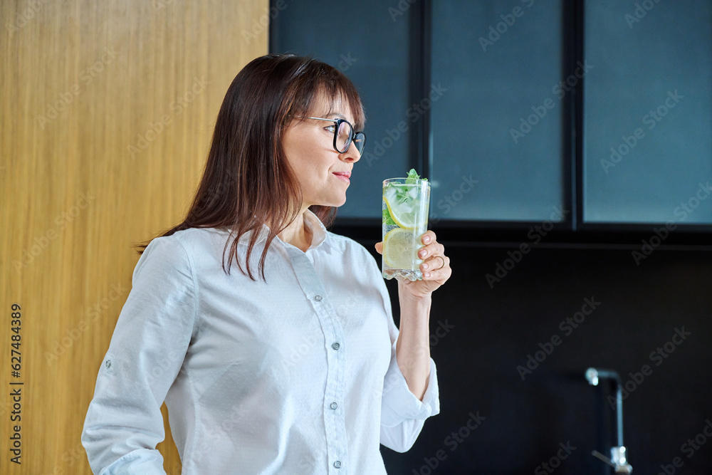Mature woman drinking glass of water with lemon ice mint Mature woman drinking glass of water with lemon ice mint