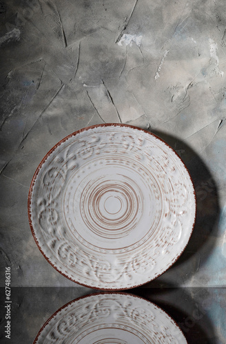 Light ceramic plate with a relief ornament against a gray wall