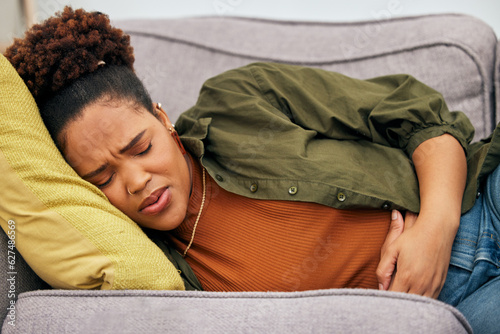 Sick woman, stomach pain and problem on sofa for ibs, health risk or nausea of gastric bloating, period cramps or virus. Black female person, menstruation or stress of constipation from endometriosis photo