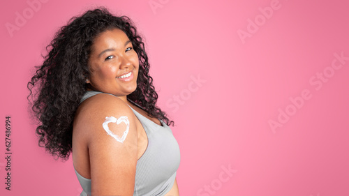 Foto Portrait of happy black plus size woman with body lotion in heart shape on shoul