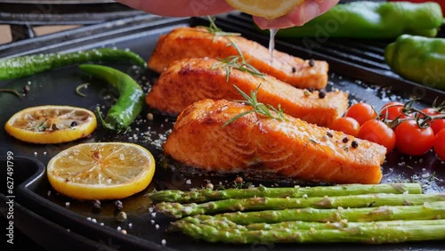 grilling fillet salmon with asparagus, tomato, lemon. A chef's hand is squeezing a fresh lemon over a peace of red sea fish. Cooking process. Slow motion. close up