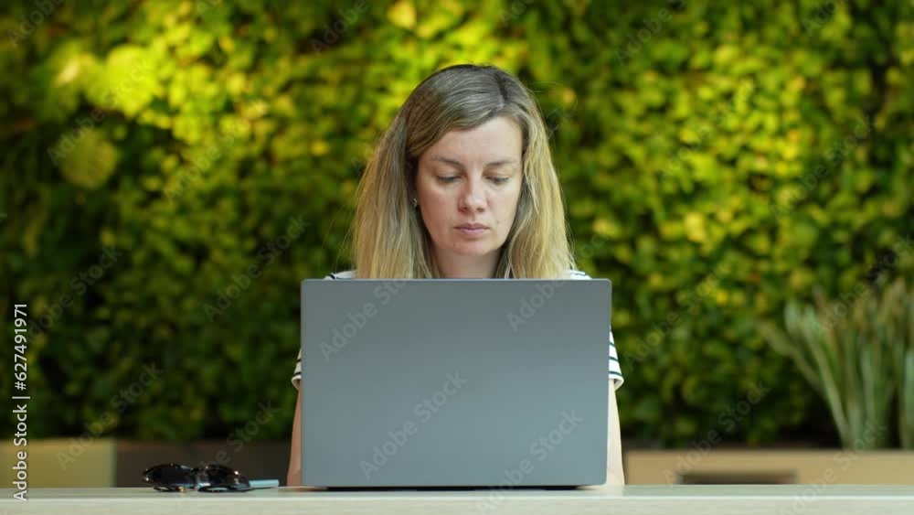 Woman using laptop in coworking with green plants. Female freelancer typing on laptop keyboard. Online work in cafe Woman using laptop in coworking with green plants. Female freelancer typing on laptop keyboard. Online work in cafe