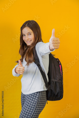 little cute schoolgirl with backpack over her shoulders keeps her fingers up in gesture up