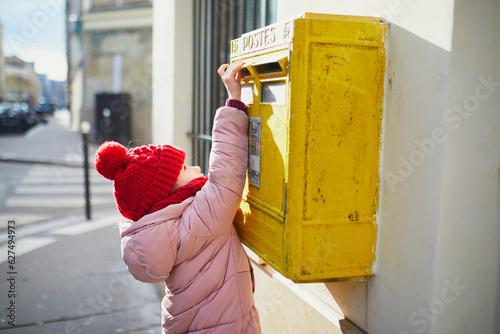 Obraz na płótnie Adorable preschooler girl putting letter in yellow post box on a street of Paris