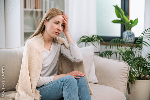 Sick woman sitting on couch, feeling cold and having headche