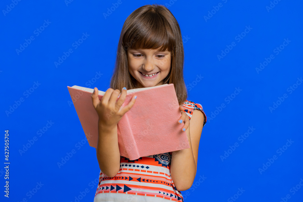 Fototapeta premium Young school girl reading funny interesting fairytale story book, leisure hobby, knowledge wisdom, education, learning, study, wow. Preteen Caucasian child kid isolated on studio blue background