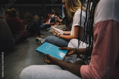 Young adults sitting at a Bible study in church looking at their bibles cropped with copy space