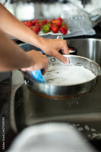 close up of a young adult male washing dishes at the kitchen sink with in a light and airy kitchen