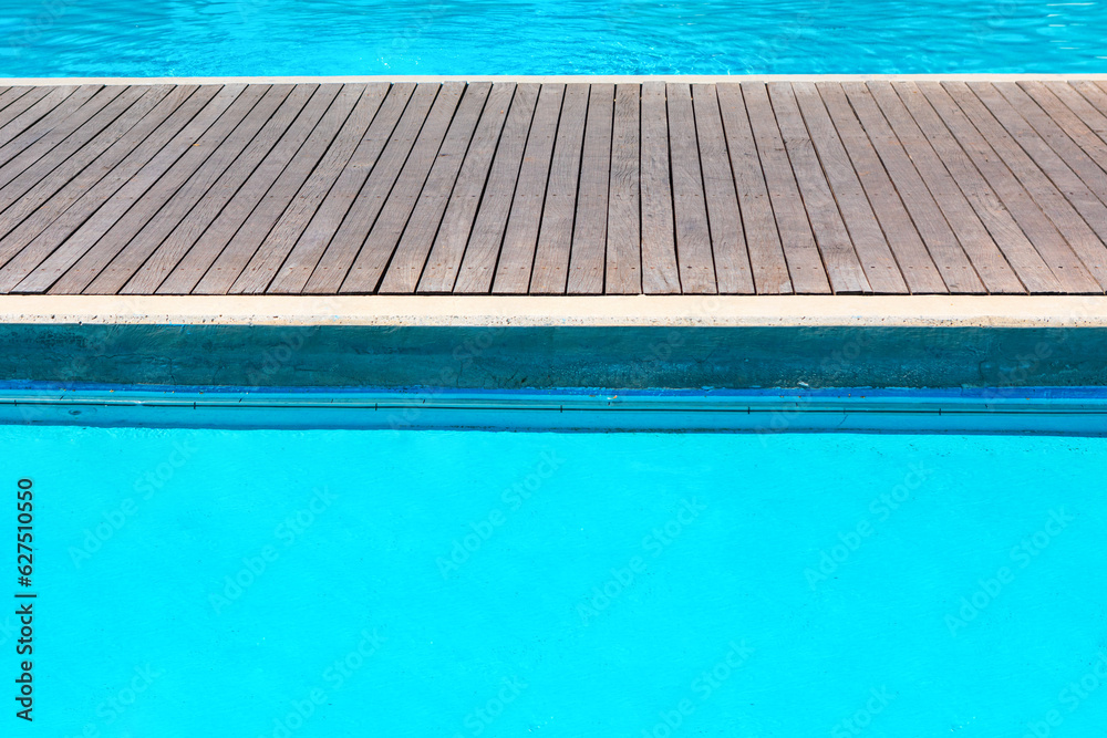 Swimming pool with wooden decking and blue water in the background