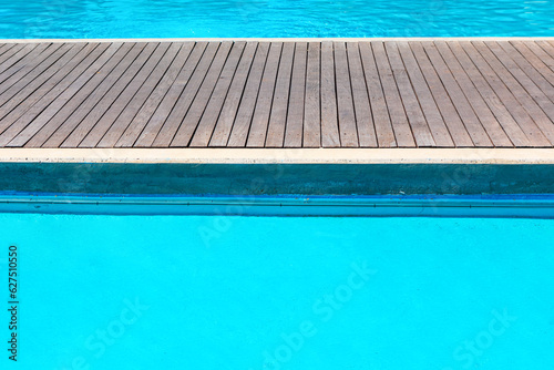 Swimming pool with wooden decking and blue water in the background