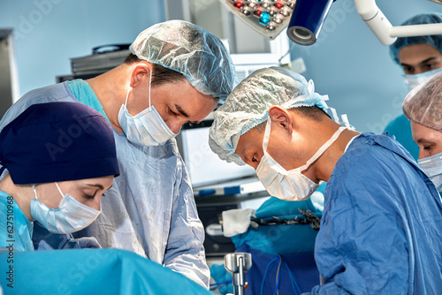 Surgeons team during complex surgical operation in a sterile operating room. Doctors leaned over patient using modern surgical instruments and clamps. Precision medicine, saving patient's life.