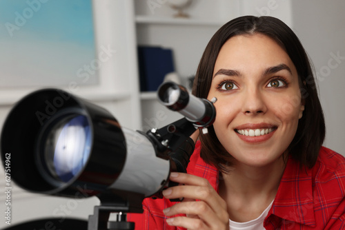 Beautiful woman using telescope to look at stars in room, closeup