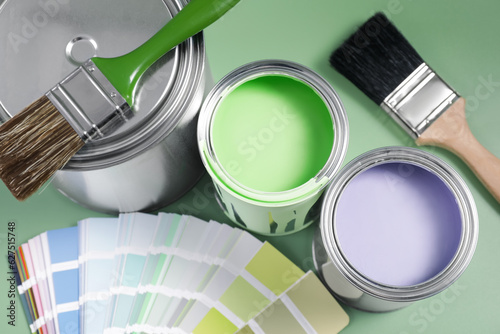 Fototapeta Naklejka Na Ścianę i Meble -  Cans of paints, palette and brushes on light green background, flat lay