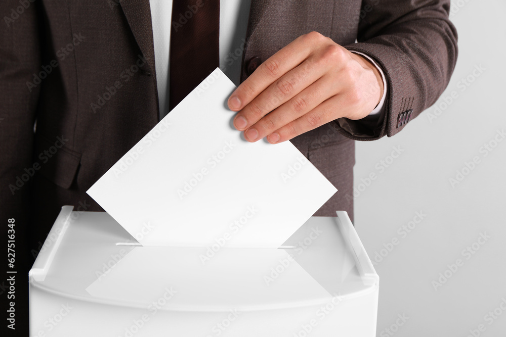 Man putting his vote into ballot box on light grey background, closeup Man putting his vote into ballot box on light grey background, closeup