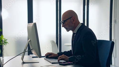 Slika na platnu Middle-aged white man in a suit working in the office with desktop PC