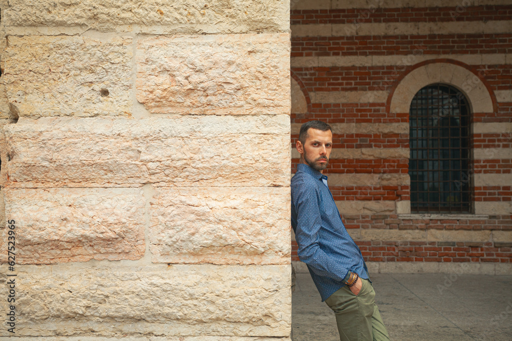 Around the world concept. Portrait of young handsome good looking man posing in the old city centre of Verona, Italy. Text space. Outdoor shot