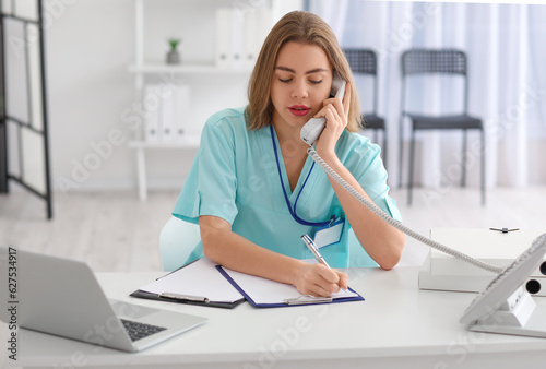 Female medical assistant talking by phone at her workplace in clinic