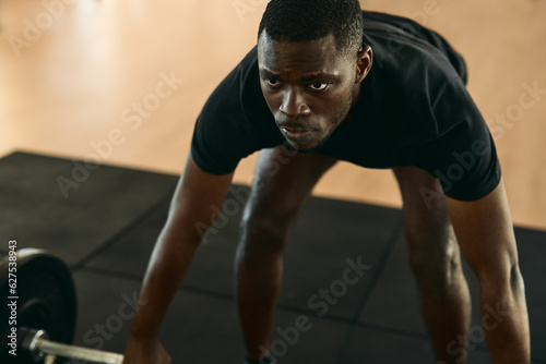 Black sportsman lifting barbell at gym